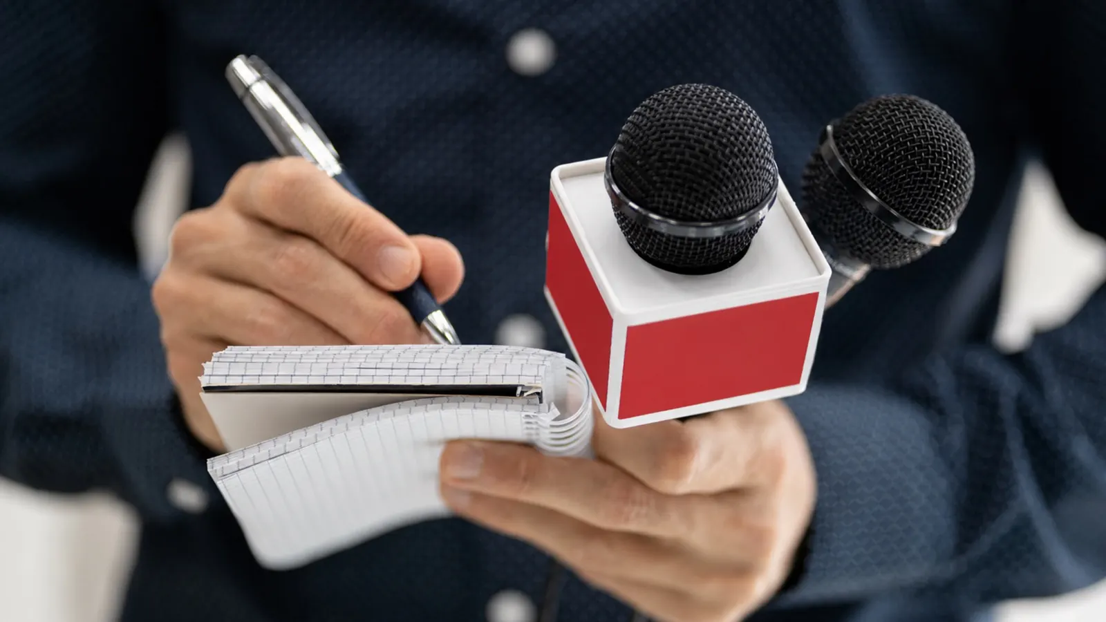 A reporter holding out microphones and a notebook for a statement